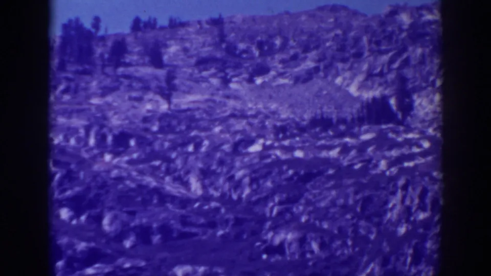 1938 Emerald Bay, California home-movie frame showing the same cliff slope, tree patches, ridge line, and aged blue-purple color cast.