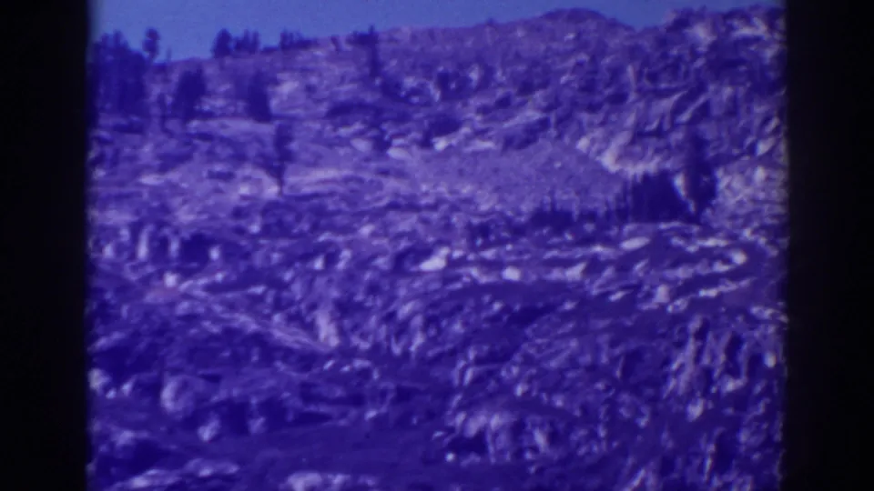 1938 Emerald Bay, California frame with rocky terrain, small evergreens, a distant ridge, clear sky, and visible 8mm scan borders.
