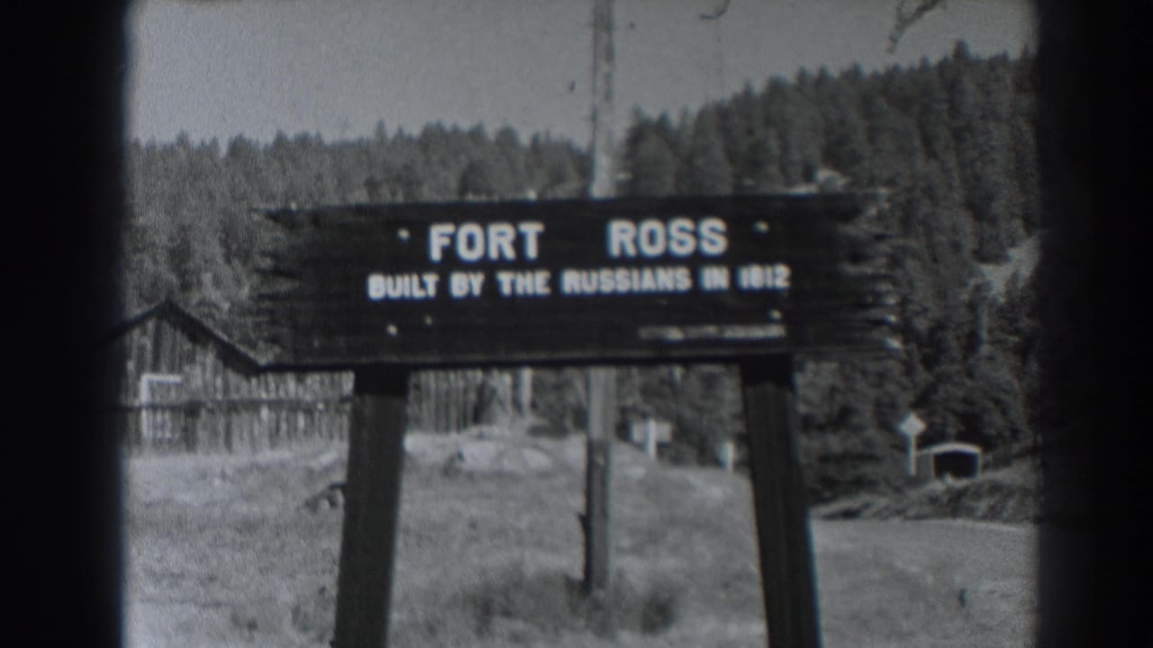 Wooden Fort Ross sign in a grassy clearing with buildings and forest behind it.