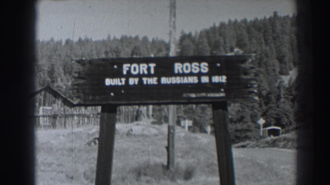Fort Ross sign with white lettering, grassy foreground, and wooded backdrop.