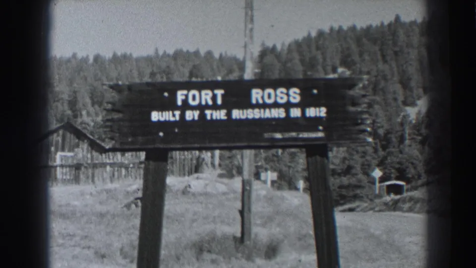 Final black-and-white frame showing the Fort Ross, California sign in a grassy clearing with a forested backdrop and small building.