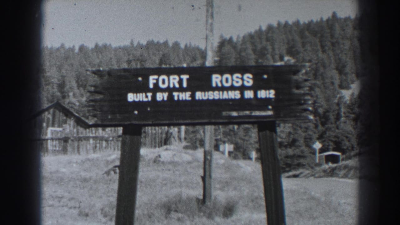 Wooden Fort Ross sign in a grassy clearing with trees and rustic buildings behind it.