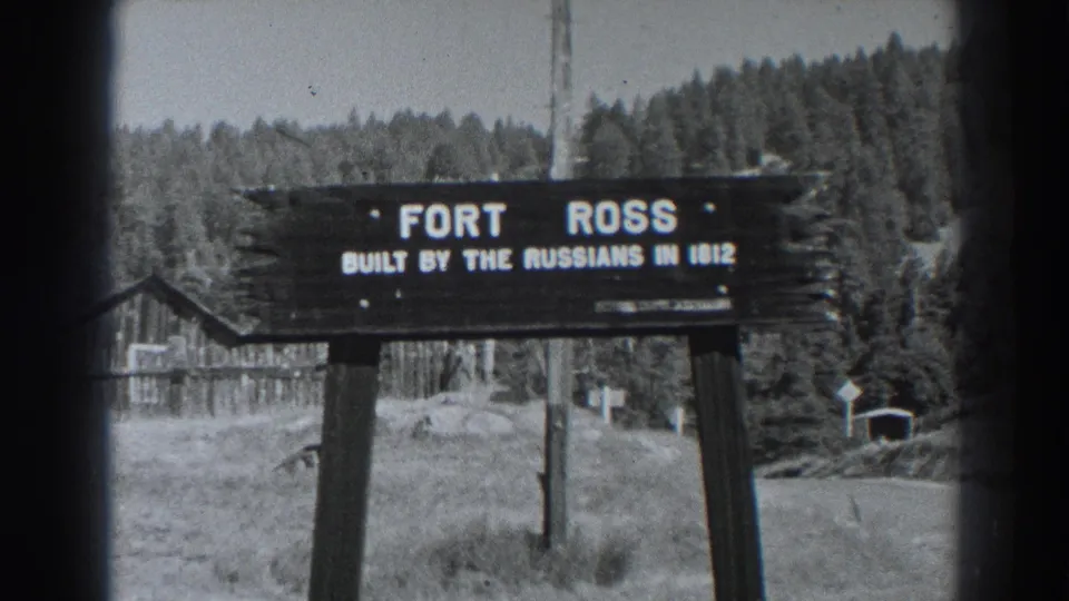 1938 8mm still of the Fort Ross sign in a rural setting, with the Russian-built date text visible and rustic structures behind.