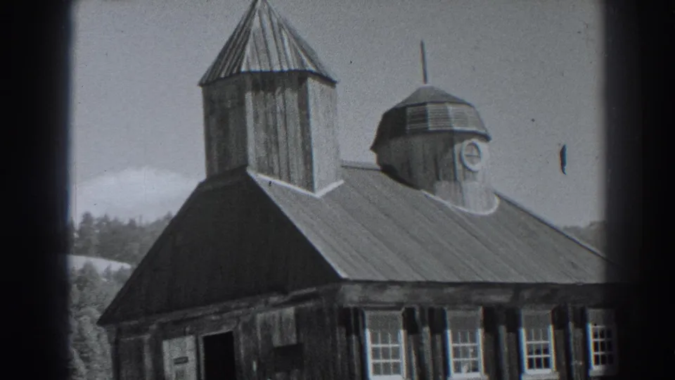 1938 Fort Ross home-movie frame showing a wooden historic building with a tall tower, cross, cupola, metal roof, windows, trees, and hillside.