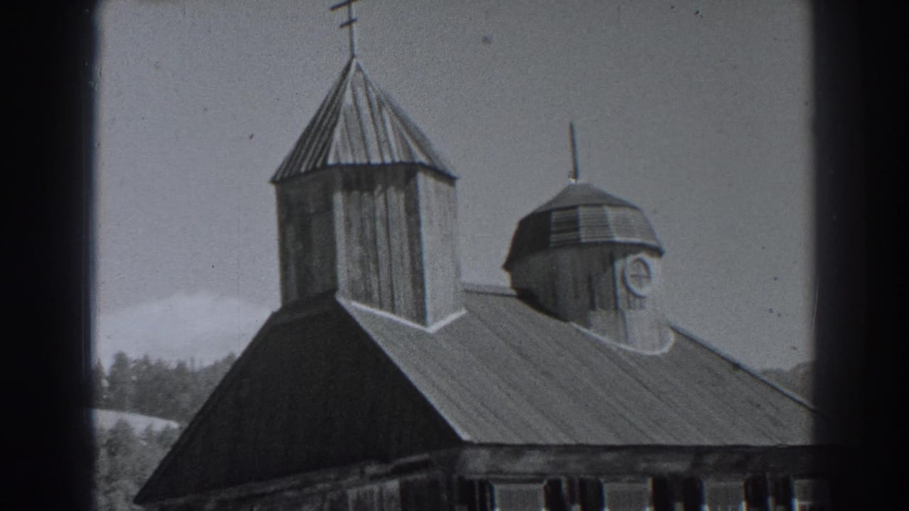 Fort Ross, California frame from 1938 showing a tall wooden tower with cross, domed cupola, sloped roof, treeline, and pale sky.
