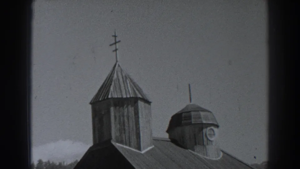 Late-1930s Fort Ross frame with the cross-topped tower, smaller cupola, metal roof, sky, and distant treeline filling the composition.