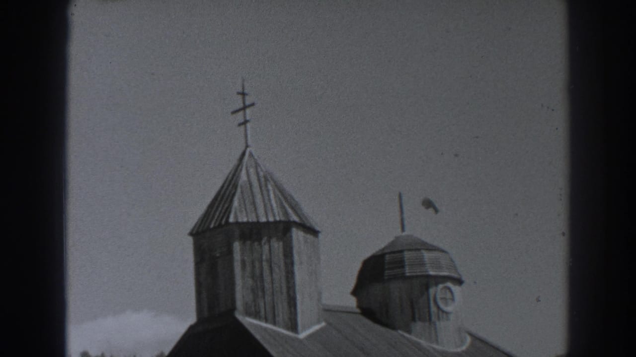 Upper portion of a wooden church with a cross-topped steeple and domed tower.