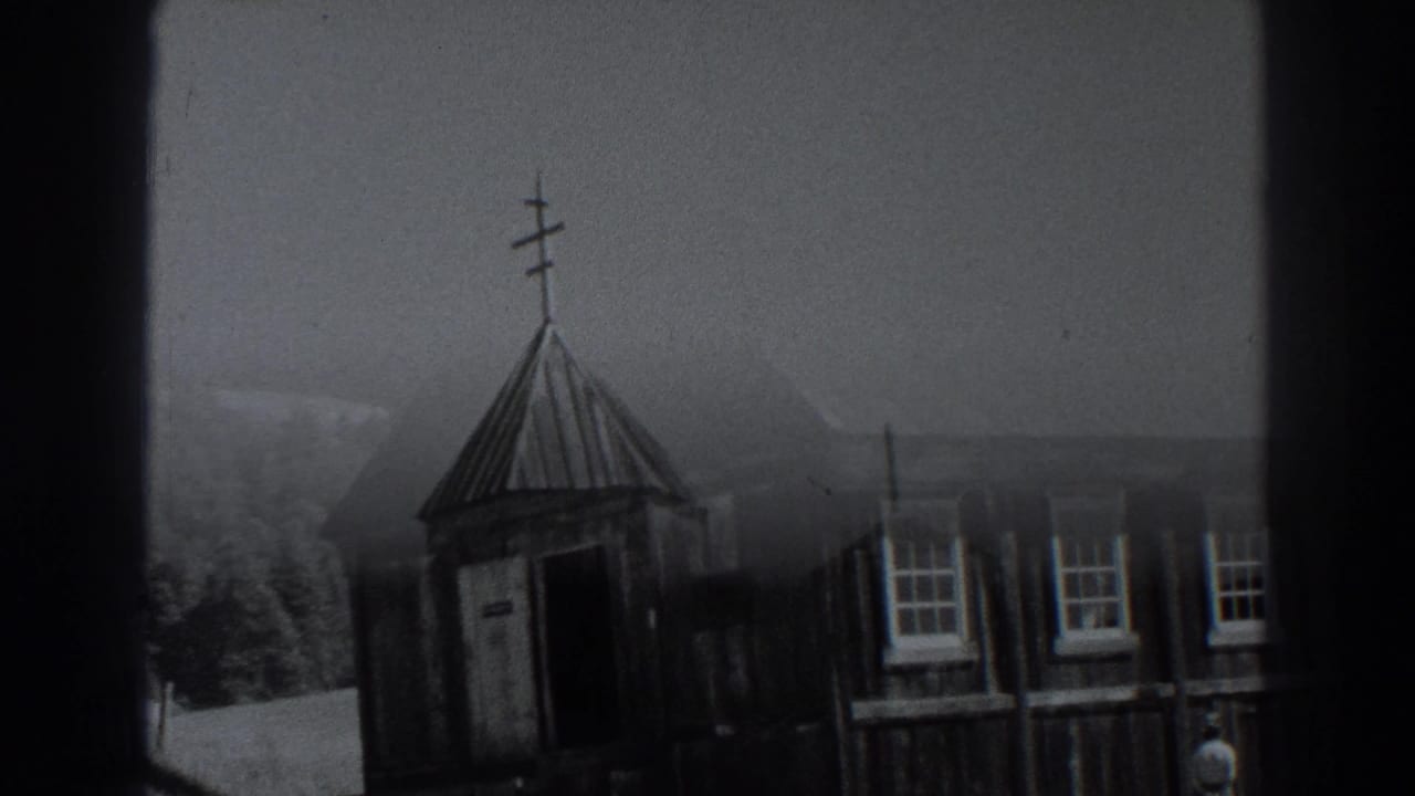 Wooden church entrance area with steeple, windows, fence, trees, and hills behind it.