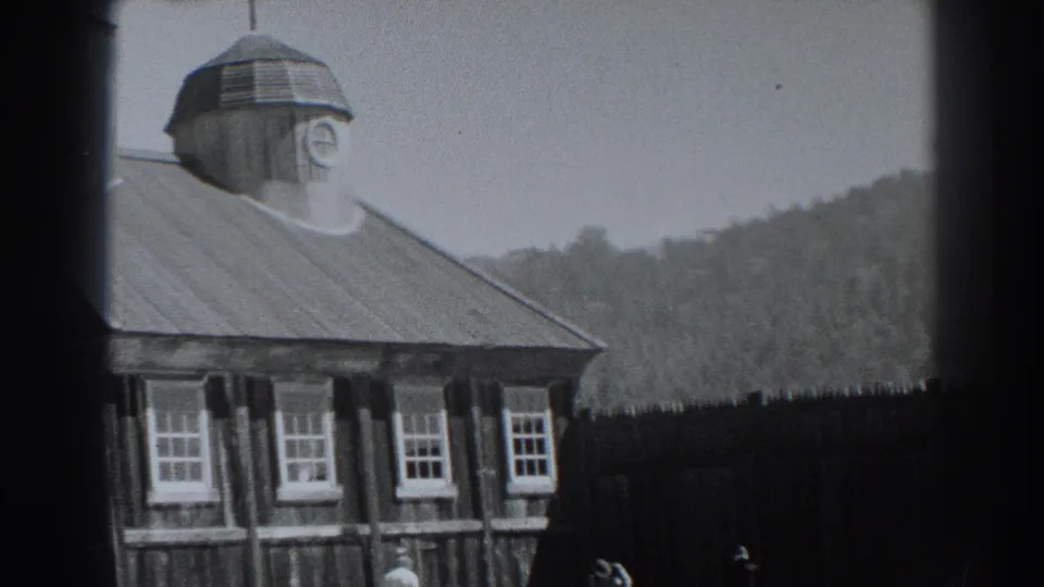 Cropped 1938 Fort Ross view emphasizing the cupola clock, roofline, rows of windows, dark foreground fence, hillside, and indistinct people.
