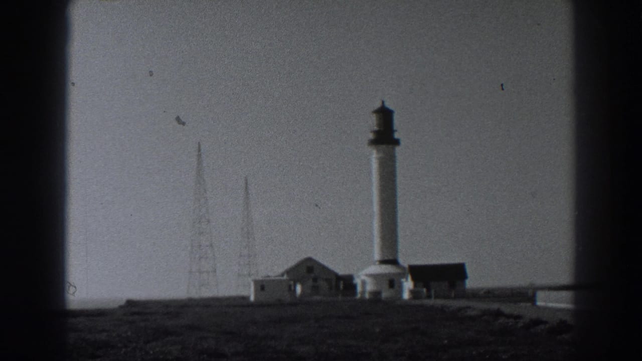 Distant lighthouse with small buildings on a coastal headland.
