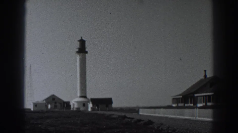 1938 Fort Ross frame showing the lighthouse, outbuildings, radio masts, low wall, and a larger structure at right.