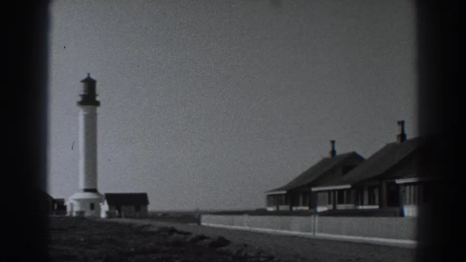 Fort Ross, California home-movie frame showing the lighthouse and adjacent beachside cottages during a slow rightward pan.