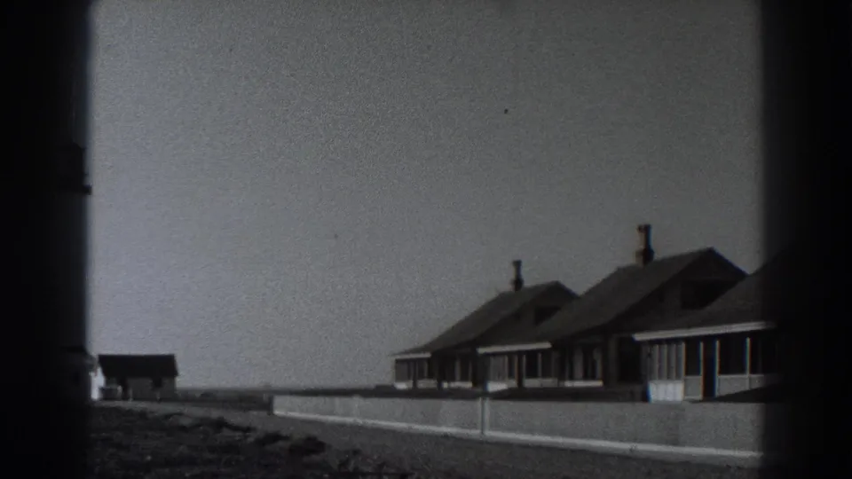 The pan moves past the Fort Ross lighthouse toward modest coastal cottages with chimneys and a low boundary wall.