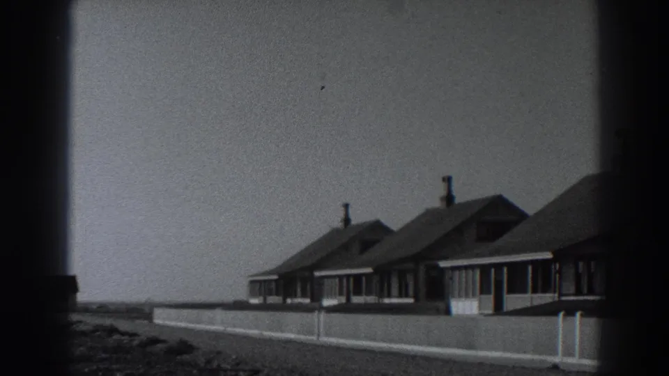 Late-frame view of the Fort Ross coastal cottages, their chimneys and rooflines framed against open sky and distant shoreline.