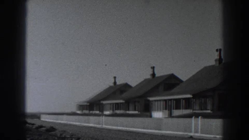 1938 Fort Ross home-movie frame showing simple seaside cottages with gabled roofs, chimneys, and a low fence.