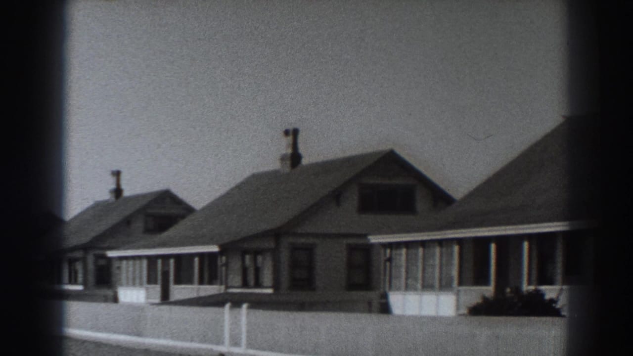 Fort Ross residential street in 1938 showing modest gabled houses, covered porches, chimneys, shrubs, and a pale fence.