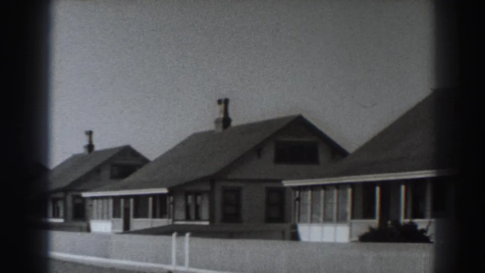 Fort Ross residential street in 1938 showing modest gabled houses, covered porches, chimneys, shrubs, and a pale fence.