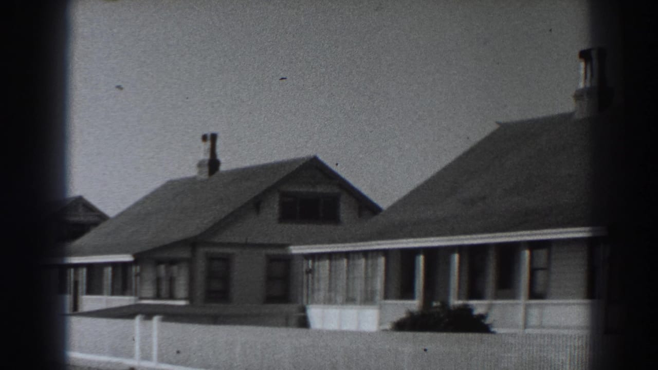 1938 Fort Ross street view with neighboring houses, porch fronts, roof chimneys, front-yard shrubs, and pale fencing.