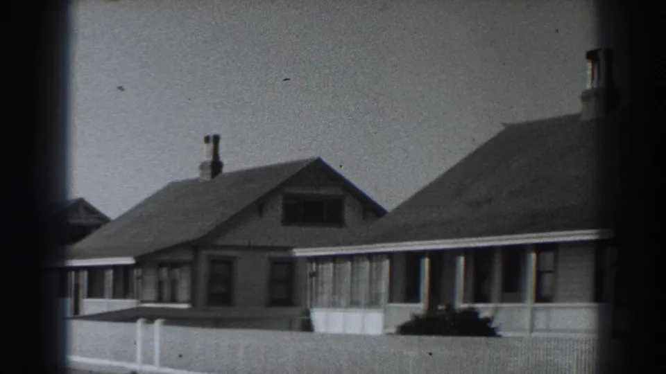 1938 Fort Ross street view with neighboring houses, porch fronts, roof chimneys, front-yard shrubs, and pale fencing.