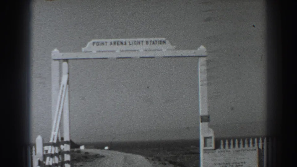1938 8mm frame showing the Point Arena Light Station entrance arch, roadside fencing, and a curved coastal approach road.