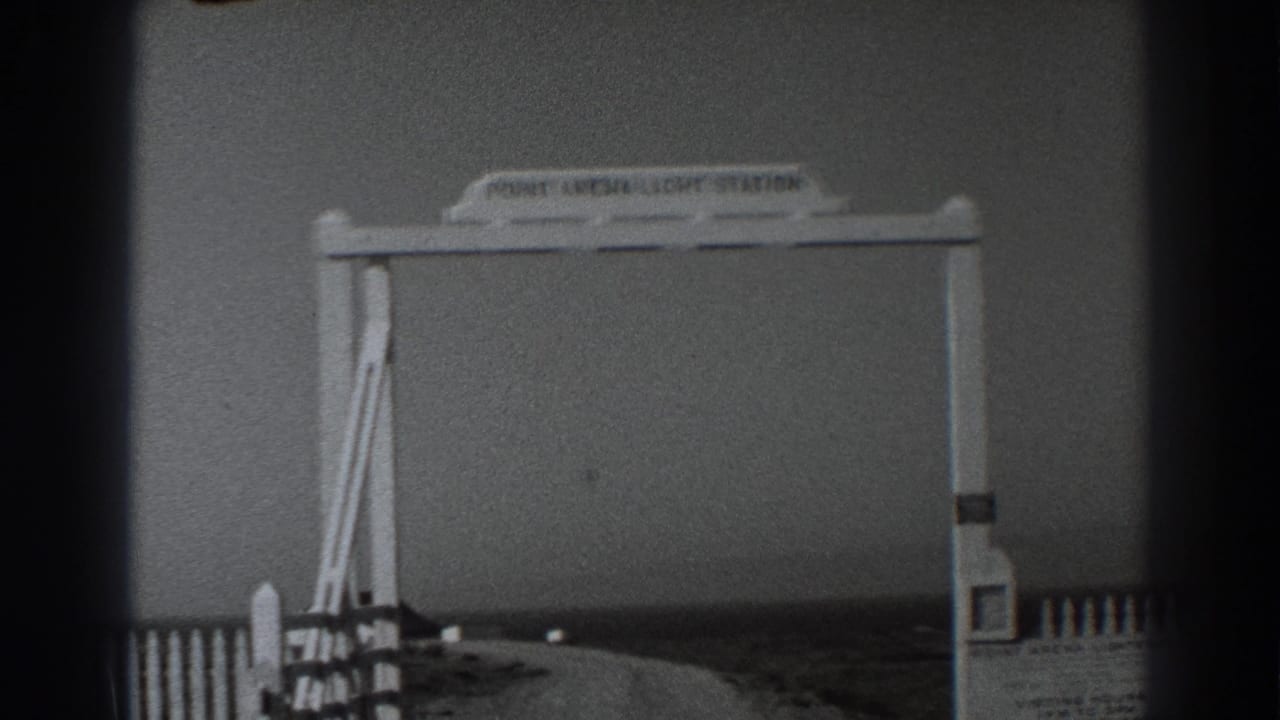 1938 8mm view of a white Point Arena Light Station entrance sign, fence, and road in a California coastal setting.