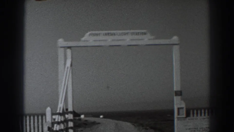 1938 8mm view of a white Point Arena Light Station entrance sign, fence, and road in a California coastal setting.