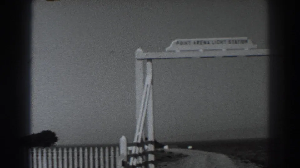 The sign and fence remain in view as the 8mm frame catches a dark foreground obstruction during the slight camera movement.
