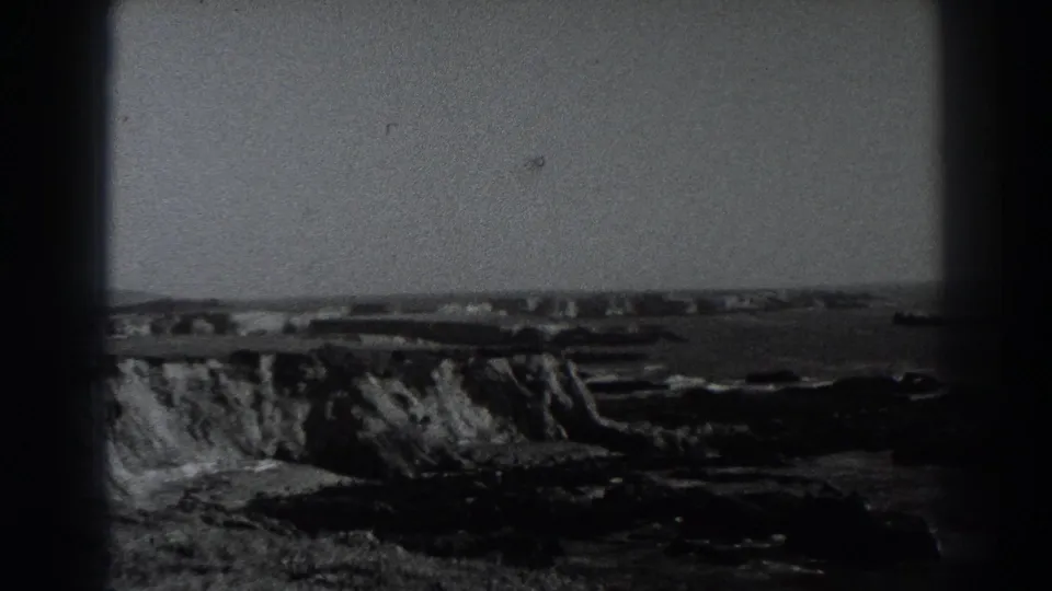 Fort Ross coastal bluff and shoreline appear beyond the film edge, with distant structures and water visible in black-and-white footage.