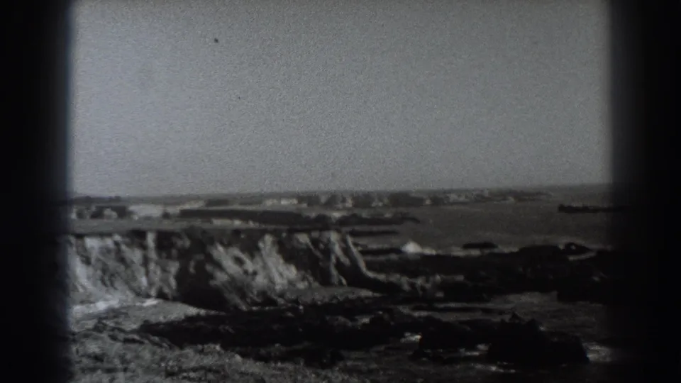 1938 Fort Ross-area 8mm frame showing rocky California cliffs, breaking surf, open sea, and faint distant shoreline features.