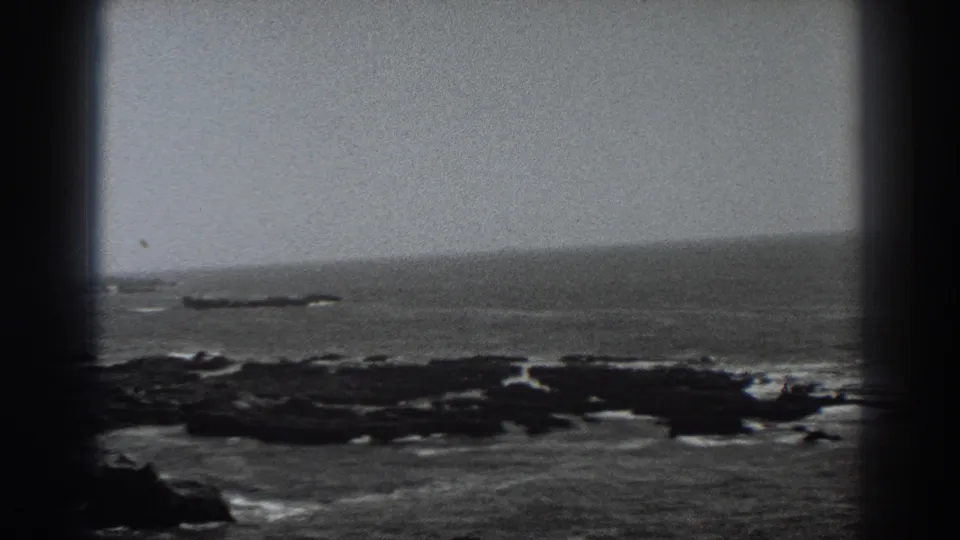 1938 Fort Ross, California 8mm frame with a stationary view of dark coastal rocks, pale surf lines, open ocean, and heavy rounded film-border shadowing.
