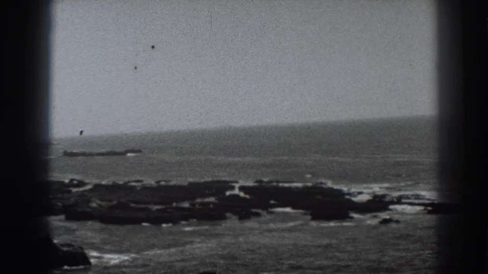 1938 Fort Ross home-movie frame showing a distant ocean horizon, rocky shoreline, and soft black-and-white 8mm texture.