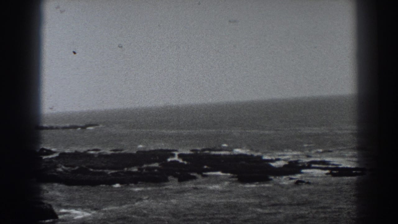 Open ocean and low rocky shoreline seen through dark film-frame borders.