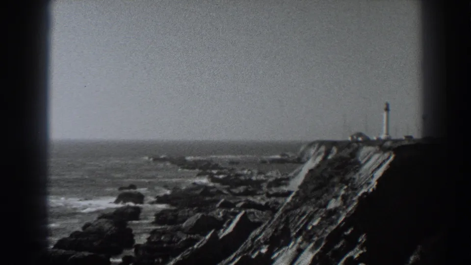 Fort Ross coastal frame showing a rocky cliff, surf below, and a lighthouse-like tower on the headland in the distance.