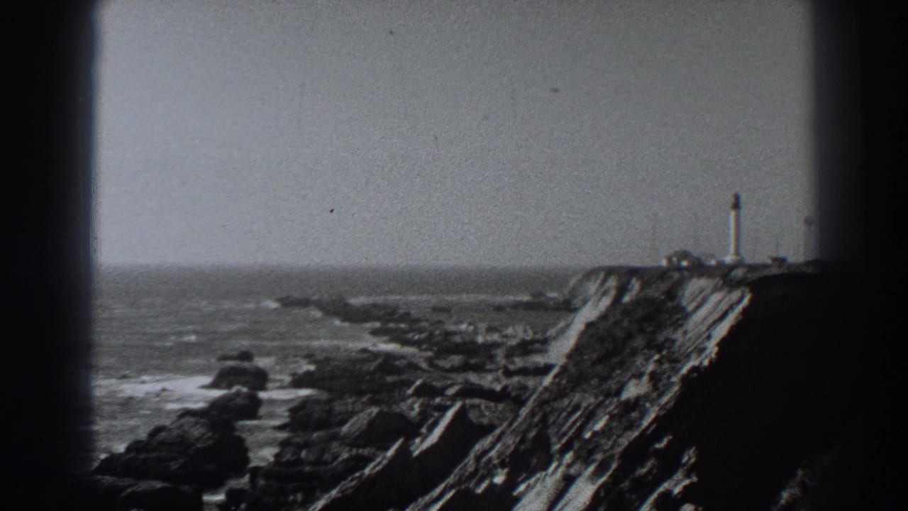 1938 Fort Ross, California home-movie frame showing a lighthouse on a rugged cliff above surf and rocks under an overcast sky.