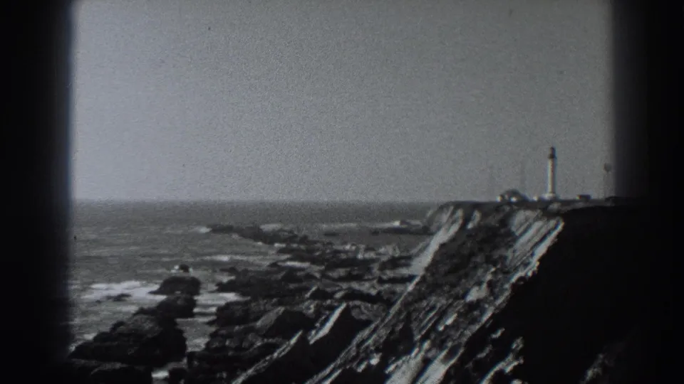 Final 1938 Fort Ross frame holding on the lighthouse above the rocky Pacific shoreline, with grain and heavy edge shadow from the film scan.