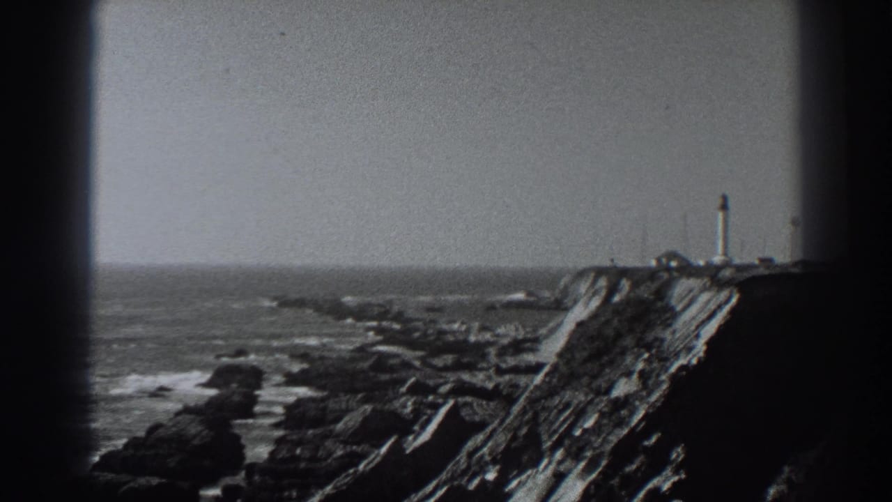 1938 Fort Ross, California home-movie frame showing a distant lighthouse-like tower on a rugged cliff above surf and rocks.