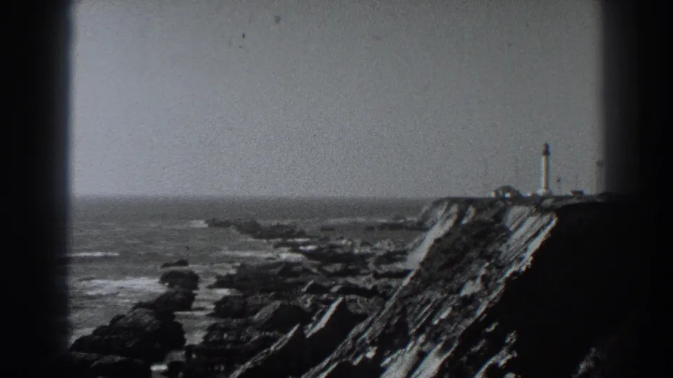 Fort Ross coastline footage frames jagged rocks, breaking waves, and a small distant tower on the cliff at right.