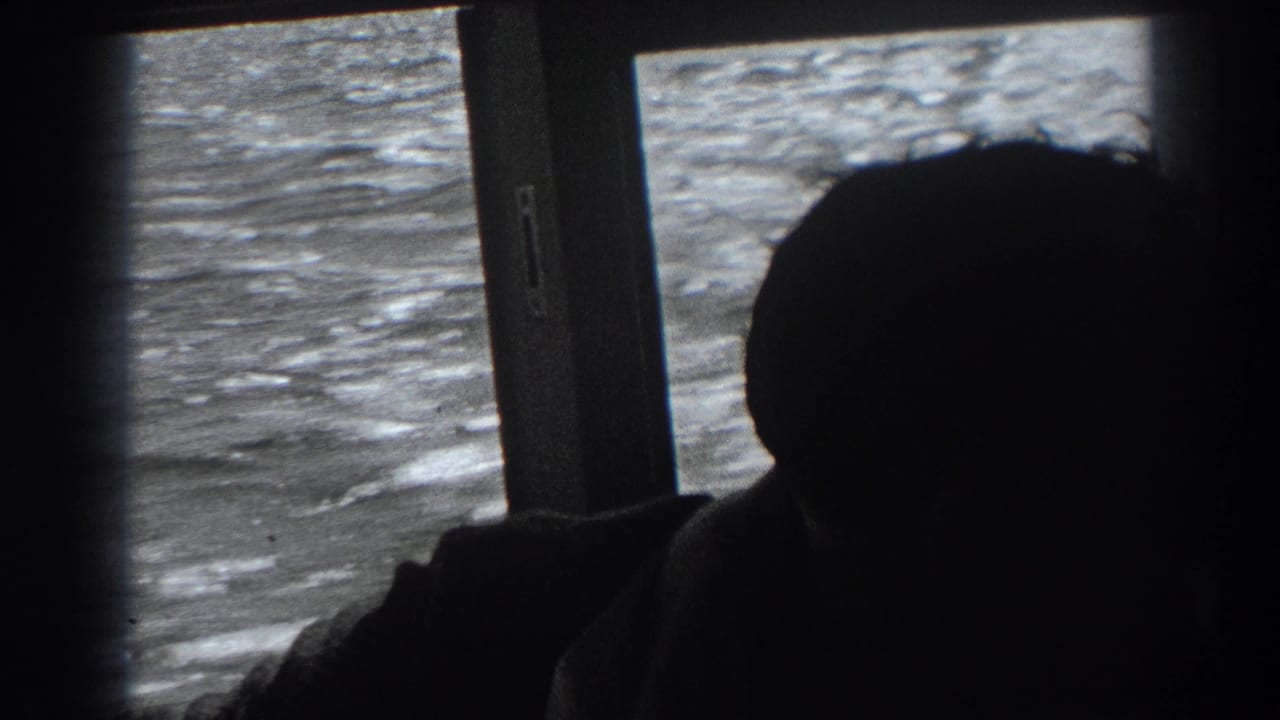 In supported 1938 Fort Ross-area home-movie footage, a balding man sits silhouetted inside a boat as sunlit water fills the window behind him.