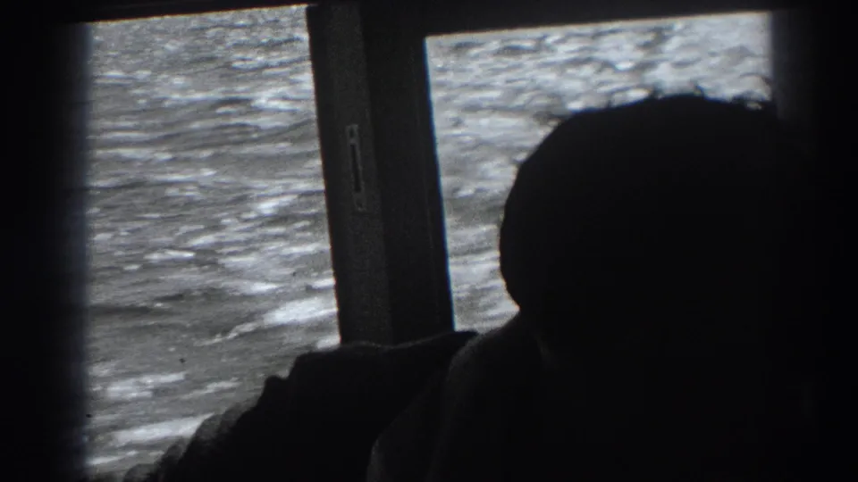 In supported 1938 Fort Ross-area home-movie footage, a balding man sits silhouetted inside a boat as sunlit water fills the window behind him.