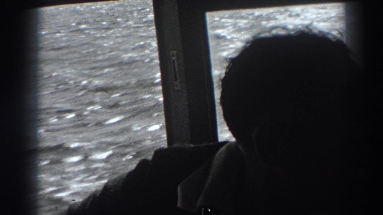 Silhouetted man sits near a boat window while textured ocean water passes outside.