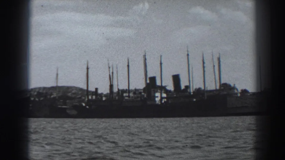 1938 Fort Ross 8mm frame showing a large docked ship in silhouette, rippled harbor water, shoreline, and cloudy sky.