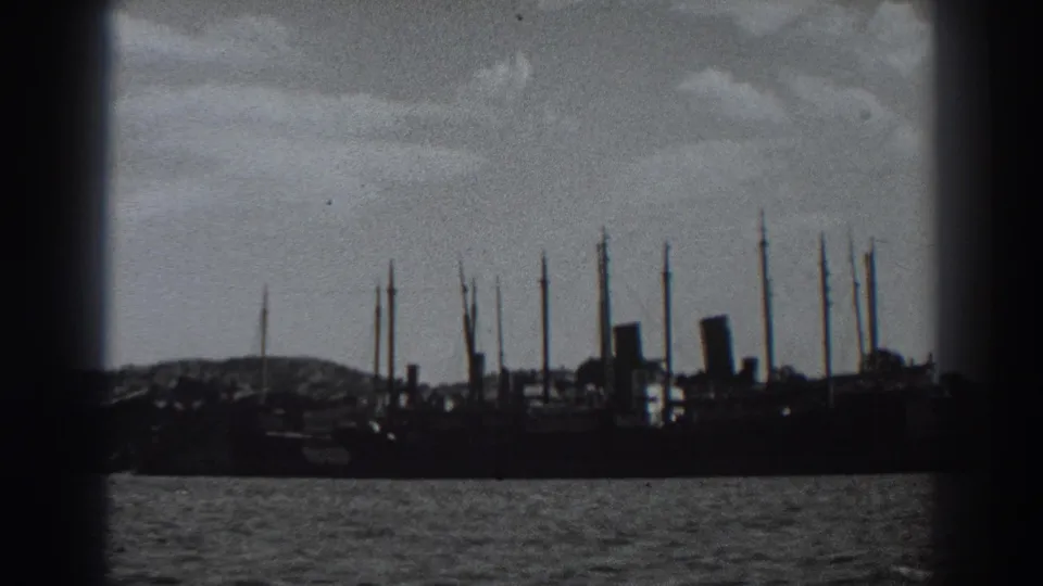 Black-and-white 8mm frame of a docked vessel at Fort Ross in 1938, with masts against the sky and water in the foreground.