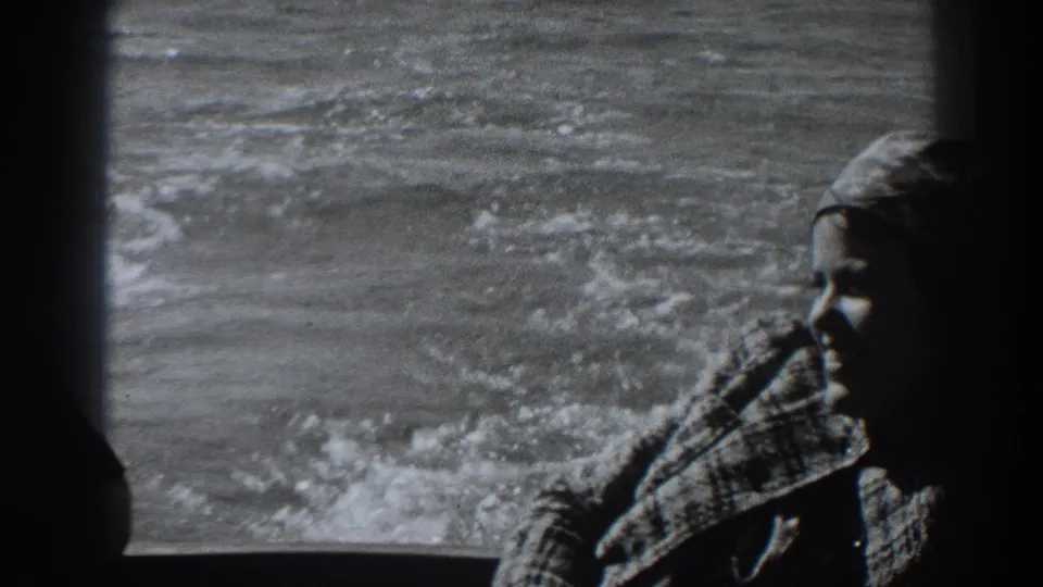 1938 8mm frame near Fort Ross showing a woman in headscarf and patterned coat beside the boat's wake.