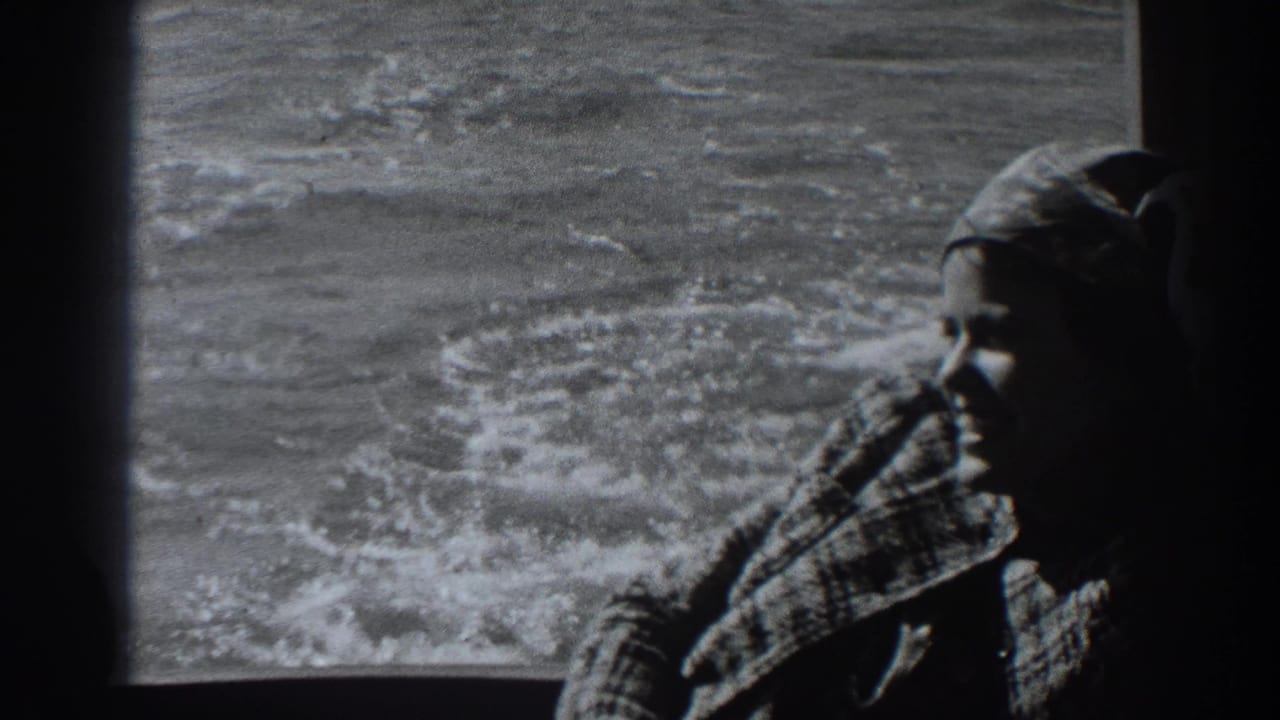 Woman in a headscarf sits by a boat window with churning water behind her.