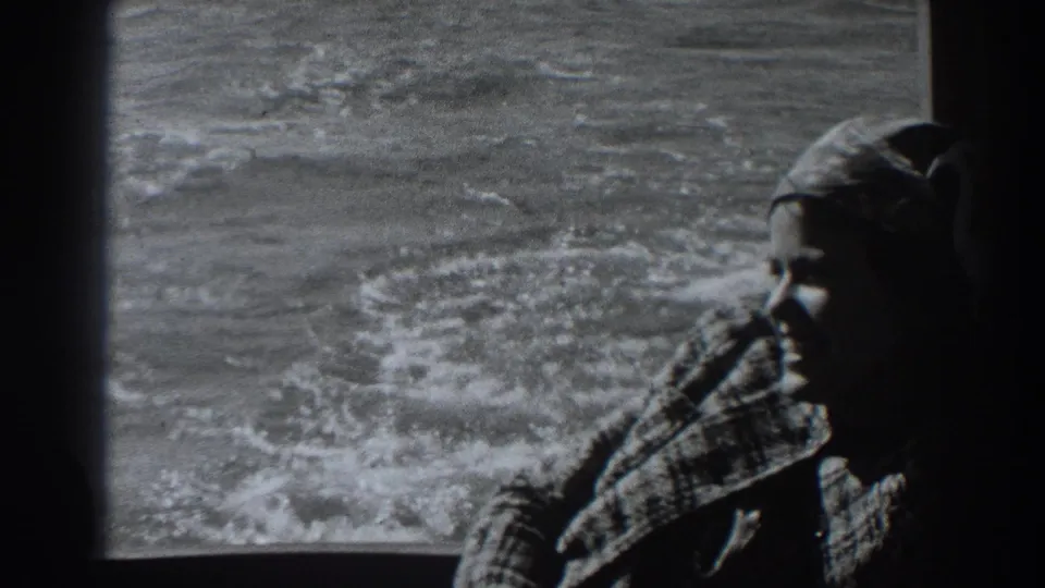 In 1938 Fort Ross-area home-movie footage, a woman in a headscarf and textured coat is framed by a boat window with wake outside.