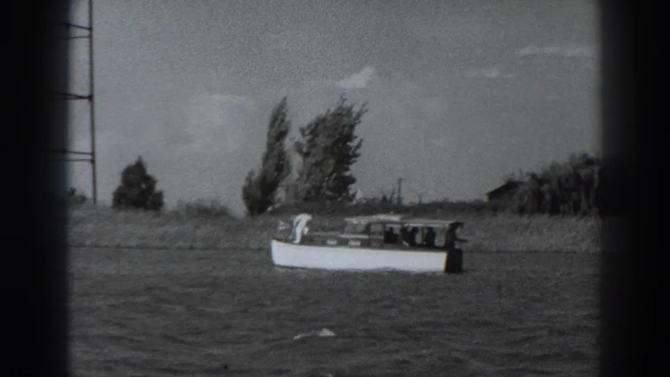 Final 1938 Fort Ross frame showing a small white motorboat on rippled water, with a rural shoreline and utility poles behind it.