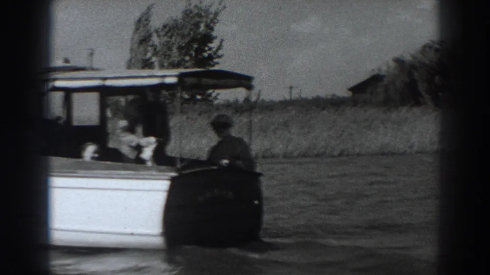 Closer 1938 8mm view of the white cabin motorboat, with passengers visible as it passes near the grassy Fort Ross shoreline.