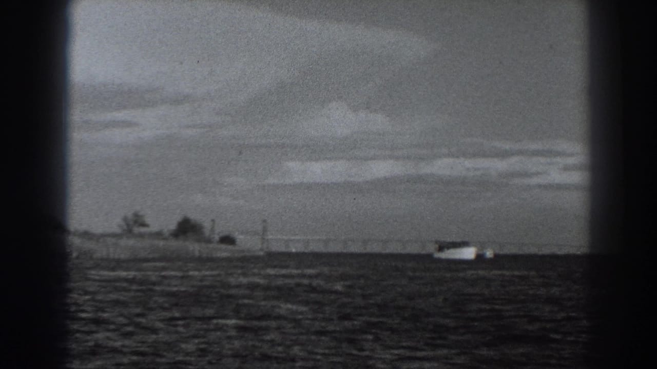 White boat near the right edge with shoreline, trees and cloud bands behind it.