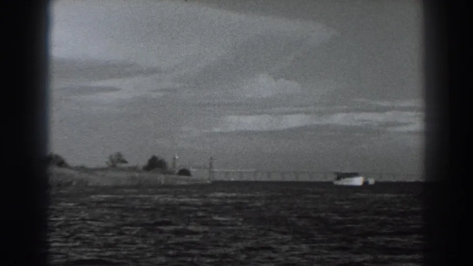 A grainy 1938 8mm view holds on rippled water, a distant boat and a sparse Fort Ross-area shoreline.