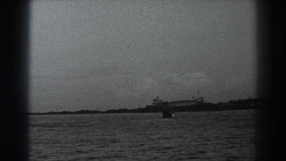 1938 Fort Ross coastal view with a larger distant ship at right, open water in front, and dark 8mm frame edges.